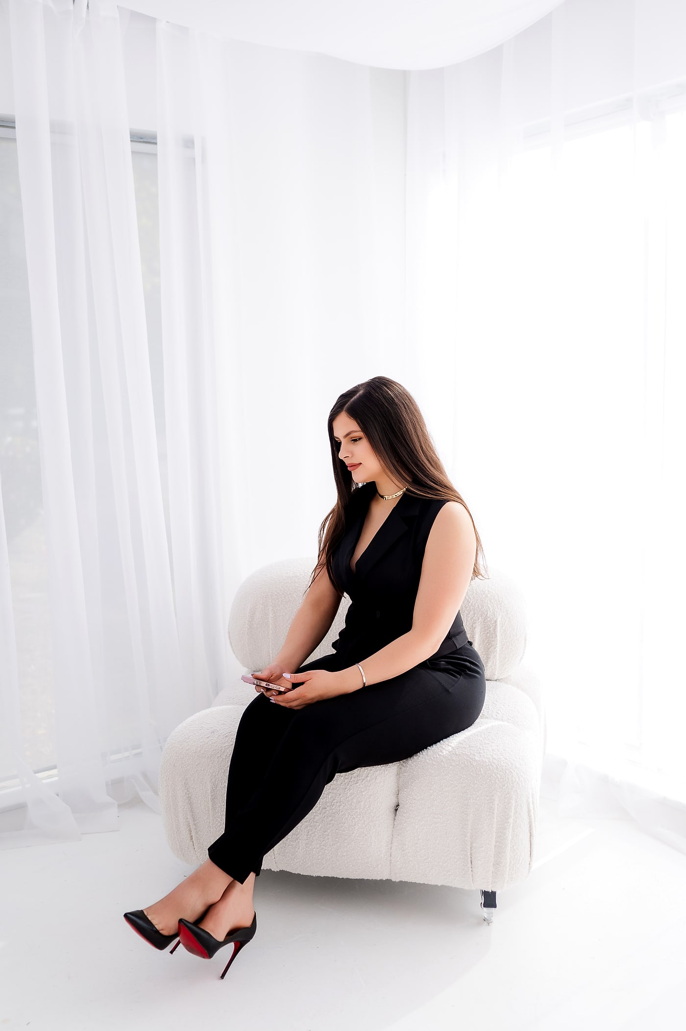 Margo Ruiz seated on a white bouclé chair beside sheer curtains, reviewing her phone